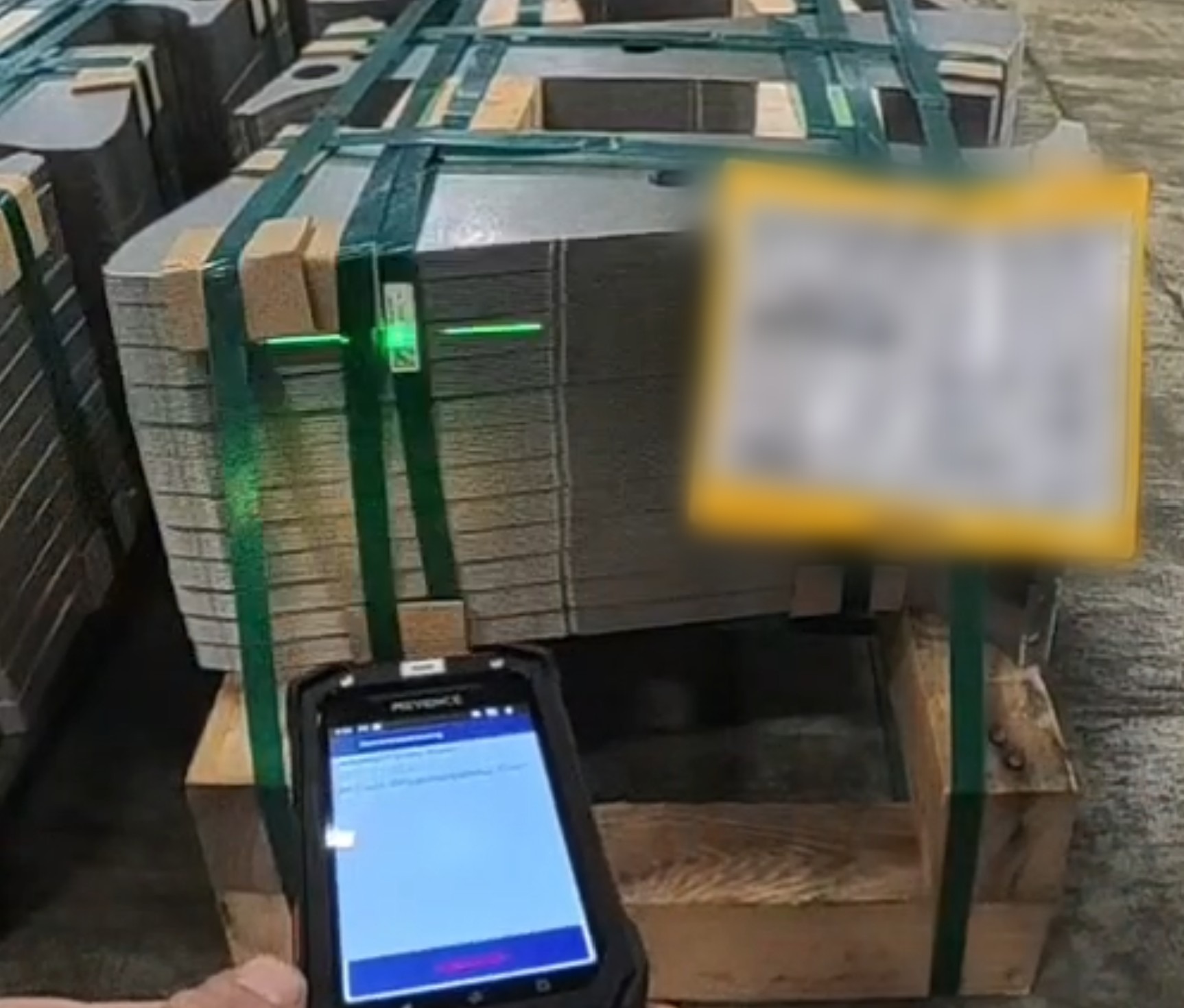 Keyence-Handheld erfasst mit grünem Ziellaser den Data-Matrix-Code direkt an einer palettierten Ladung Metallplatinen